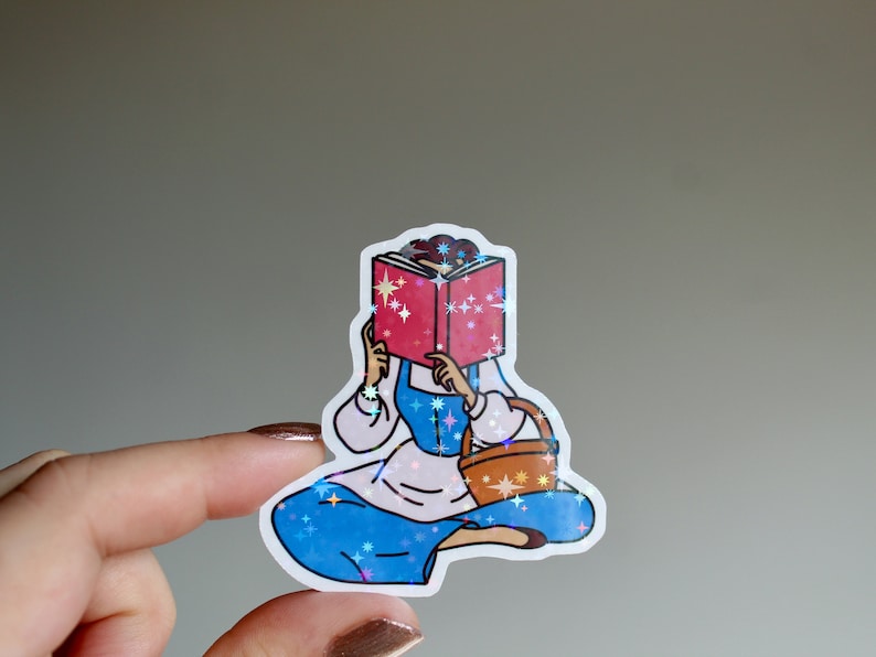 May include: A sticker of a cartoon woman reading a book with a basket in her hand. The sticker has a sparkly, iridescent finish.