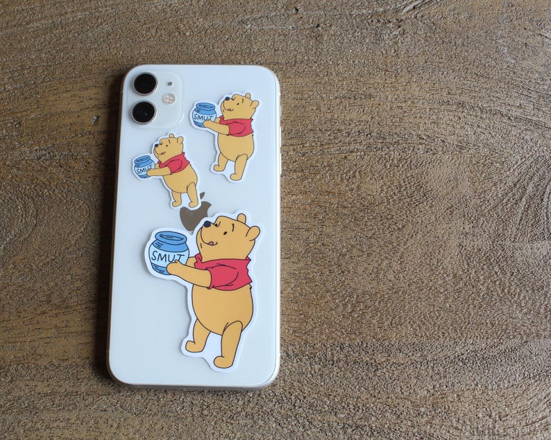 May include: Three Winnie the Pooh phone stickers. Each sticker features Winnie the Pooh holding a jar of honey that says "SMUT" on it. The stickers are on a white iPhone.