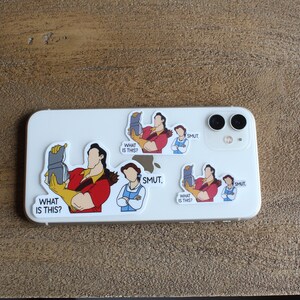 K&ouml;nnte beinhalten: Eine wei&szlig;e iPhone-H&uuml;lle mit mehreren Aufklebern. Die Aufkleber zeigen Comicfiguren aus dem Disney-Film Die Sch&ouml;ne und das Biest. Der Text auf den Aufklebern lautet "What is this?" und "SMUT."