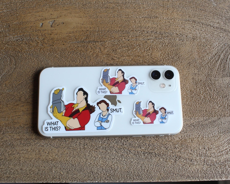 K&ouml;nnte beinhalten: Eine wei&szlig;e iPhone-H&uuml;lle mit mehreren Aufklebern. Die Aufkleber zeigen Comicfiguren aus dem Disney-Film Die Sch&ouml;ne und das Biest. Der Text auf den Aufklebern lautet "What is this?" und "SMUT."