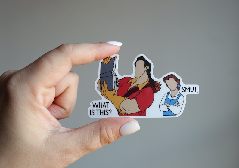 K&ouml;nnte beinhalten: Ein Aufkleber mit einer Cartoon-Illustration von Belle und dem Biest aus Disneys Die Sch&ouml;ne und das Biest. Das Biest h&auml;lt ein Buch und sagt "What is this?" Belle steht mit verschr&auml;nkten Armen da und sagt "Smut."