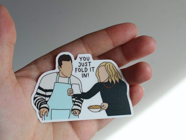 May include: A sticker featuring a cartoon illustration of two people, one holding a bowl of cereal and the other holding a mug. The text on the sticker reads "You just fold it in!"