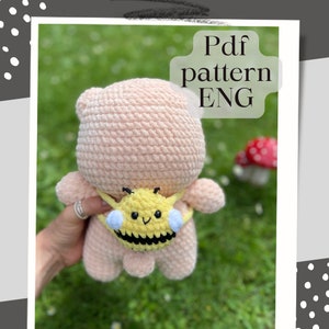 May include: A pink crocheted bear with a yellow and black crocheted bee backpack. The bee has a smiling face and white wings. The text "Pdf pattern ENG" is in the upper right corner of the image.