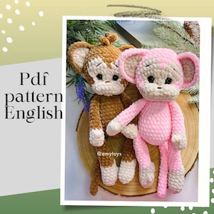 Puede incluir: Dos juguetes de mono de crochet, uno marrón y otro rosa, sentados sobre una superficie de madera. Los juguetes tienen detalles de hilo blanco y están hechos con un hilo esponjoso. La leyenda de la imagen dice "Pdf pattern English @emytoys".