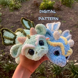 May include: Two crocheted dragon plushies, one green and one blue, with white accents and large eyes. The text "DIGITAL PATTERN" is visible above the plushies.