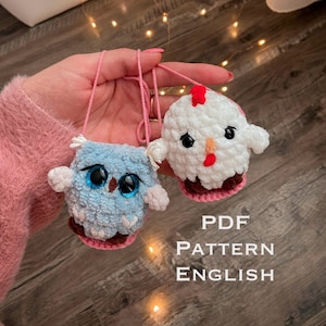 Peut inclure: Deux jouets en peluche crochetés : un hibou bleu avec de grands yeux bleus et une poule blanche avec une crête rouge. Les deux ont des boucles de ficelle roses. Le texte "PDF PATTERN ENGLISH" est en dessous.
