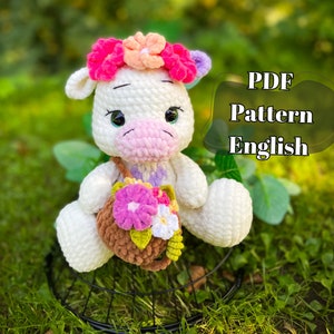 Può includere: Schema all'uncinetto per una mucca di peluche bianca con naso e zoccoli rosa, che indossa una corona di fiori e porta un cestino di fiori. Lo schema è in inglese e disponibile per il download in PDF.
