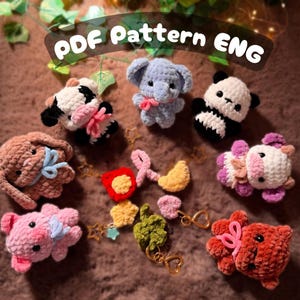 Può includere: Una collezione di piccole figure di animali all'uncinetto in peluche, tra cui una mucca, un elefante, un panda, un coniglio e un maiale, insieme a vari ciondoli all'uncinetto come stelle, cuori e un quadrifoglio. Il testo PDF PATTERN ENG è visibile.