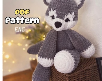 Può includere: Un peluche a forma di lupo all'uncinetto grigio e bianco fatto a mano. Il lupo ha un naso nero, dettagli bianchi intorno agli occhi e alla bocca e zampe bianche. Il testo "PDF Pattern ENG" si trova nell'angolo in alto a sinistra. Il peluche è su un cestino intrecciato.