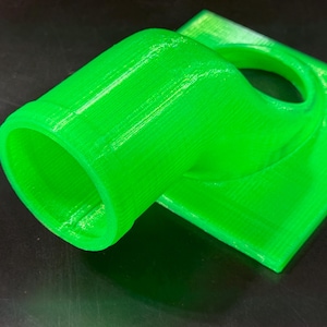 May include: A bright green 3D printed plastic adapter with a round opening on one end and a flat surface on the other.