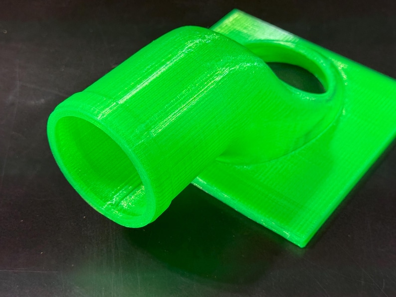 May include: A bright green 3D printed plastic adapter with a round opening on one end and a flat surface on the other.