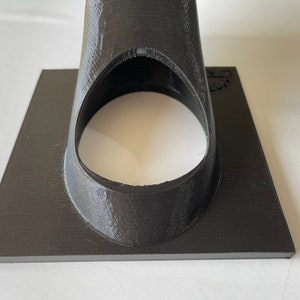 May include: A black 3D printed object with a circular opening. The object has a flat base and a cone-shaped top.