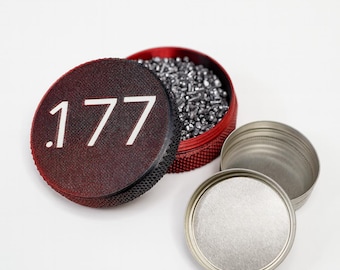 May include: A red and black container of .177 calibre pellets, with a lid displaying the number .177 in white. The container is open, revealing the pellets inside. Two additional silver lids are also present.