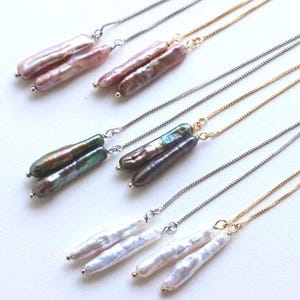 May include: Six pairs of threader earrings featuring elongated, irregular stick-shaped freshwater pearls in shades of pink, dark iridescent green, and white, attached to delicate silver-tone and gold-tone box chains with small metal end beads.