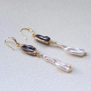 May include: A pair of gold drop earrings. Each earring has a dark, irregularly shaped stone set in gold, connected to a long, white, oblong pearl. The earrings have a hook closure.
