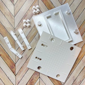 May include: White plastic molds for making soap, with a variety of shapes and sizes. The molds are arranged on a wooden surface.