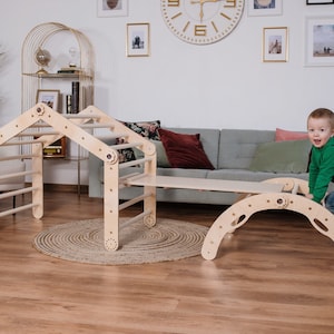 May include: A wooden play structure for children, featuring a climbing wall, a slide, and a tunnel. The structure is made of natural wood and has a light brown finish. A young child is playing on the structure, climbing up the wall and sliding down the slide.