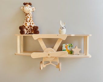 May include: Wooden airplane shelf with two shelves, a giraffe stuffed animal, a bunny figurine, a star, and a book on the top shelf.