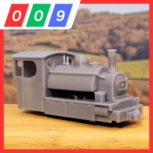 Puede incluir: Un modelo de tren gris con un diseño detallado, que incluye una chimenea, cabina y ruedas. El tren se encuentra sobre un fondo borroso de un paisaje. La imagen incluye los números 0, 0 y 9 en rojo, verde y azul.