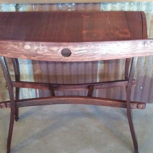 May include: A dark brown wooden table with a curved top and a unique, open-frame base. The table is made from reclaimed wood and has a rustic, farmhouse style.