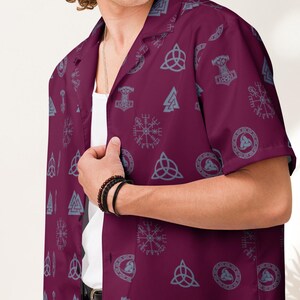 May include: A burgundy short-sleeved button-up shirt with a pattern of gray Norse symbols, including the Valknut, the Triskele, and Thor's hammer.