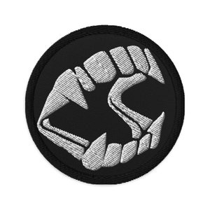 May include: A black and white embroidered patch with a white image of a set of fangs on a black circle.