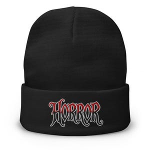 May include: Black beanie with the word "HORROR" embroidered in red with a white outline. The beanie is a classic style, with a folded cuff. The text is in a gothic font.