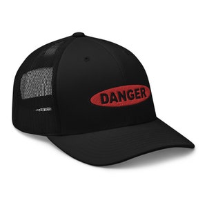 Op de afbeelding: Zwarte truckercap met een rood ovaal patch waarop in zwarte letters "DANGER" staat.