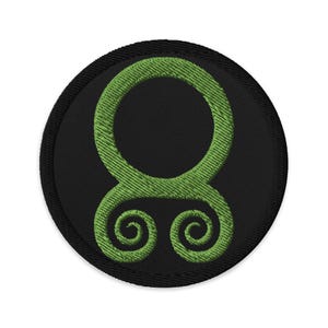 May include: Green embroidered patch with a circular design on a black background. The design features a large circle with two smaller circles at the bottom.