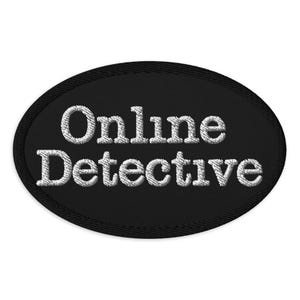 May include: An oval patch featuring the text "Online Detective" in white embroidered lettering on a black background. The patch has a black border and a textured finish.