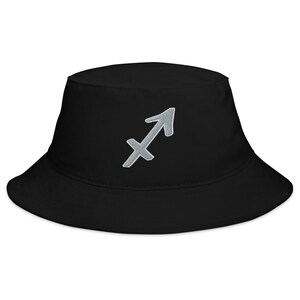 Puede incluir: Un gorro de pescador negro con un símbolo de Sagitario del zodíaco plateado bordado en la parte delantera.