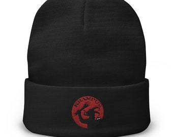May include: Black knit beanie with a red embroidered circle featuring a silhouette of Krampus, a mythical creature, holding a bundle of birch branches. The text "Krampus" is written around the circle.