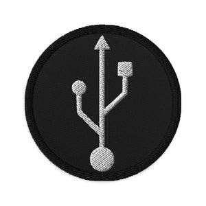 May include: A black and white embroidered patch featuring a USB symbol. The patch is circular and has a black border.