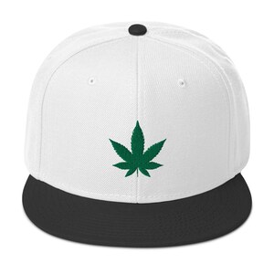 May include: A white and black baseball cap with a green marijuana leaf embroidered on the front.