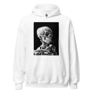 Puede incluir: Sudadera con capucha blanca con una pintura en blanco y negro de un esqueleto fumando un cigarrillo. La obra de arte está centrada en la parte delantera de la sudadera. La sudadera tiene una capucha con cordón y un bolsillo de canguro.