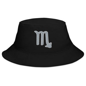 Puede incluir: Sombrero de pescador negro con un símbolo de Escorpio bordado en plata.