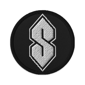 Op de afbeelding: Geborduurde patch met het iconische "S"-ontwerp, een gestileerde letter bestaande uit in elkaar grijpende vormen. De patch heeft een zwarte cirkelvormige rand en een wit, getextureerd "S"-ontwerp in het midden.