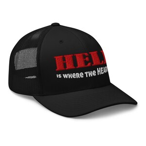 May include: Black trucker hat with the embroidered text "HELL" in red, above the phrase "is where the HEAR" in white. The hat features a mesh back panel and a curved brim.