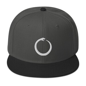Könnte beinhalten: Eine dunkelgraue und schwarze Baseballkappe mit einem weißen gestickten Kreis, der ein Schlangendesign enthält.