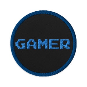 May include: A blue and black round embroidered patch with the word "GAMER" in pixelated blue letters.