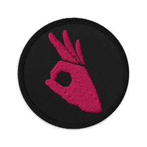 Pode incluir: Patch bordado com um gesto de mão rosa sobre um fundo circular preto. A mão forma o símbolo "ok", com o polegar e o indicador tocando-se. O patch tem uma borda preta.