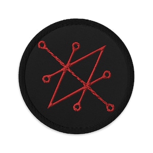 Può includere: Una toppa rotonda nera ricamata con un disegno di sigillo rosso. Il sigillo è composto da linee e cerchi intersecanti, creando un motivo geometrico. La toppa ha un bordo nero ed è adatta per abbigliamento o accessori.