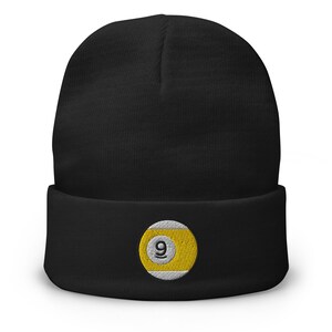 May include: Black beanie with a yellow and white embroidered patch featuring the number 9, commonly associated with the game of pool. The beanie is made of a soft, knitted material and has a folded cuff.