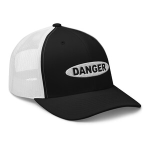 Op de afbeelding: Zwarte en witte truckercap met een witte ovale patch waarop in zwarte letters "DANGER" staat.