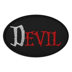 May include: Oval black embroidered patch with the word "DEVIL" in white and red gothic lettering. The patch has a black border and is likely designed to be sewn onto clothing or accessories.