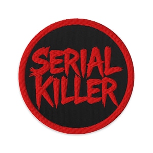 May include: Round embroidered patch with the words "SERIAL KILLER" in red, stylized lettering on a black background. The patch has a red border and is likely designed to be sewn or ironed onto clothing or accessories.