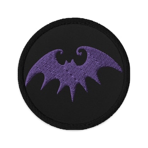 以下が含まれることがあります： 黒い円形のワッペンに紫色の刺繍されたコウモリ