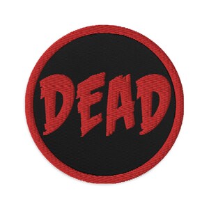 Könnte beinhalten: Ein roter gestickter Aufnäher mit schwarzem Hintergrund und dem Wort "DEAD" in einer fetten, stilisierten Schrift.