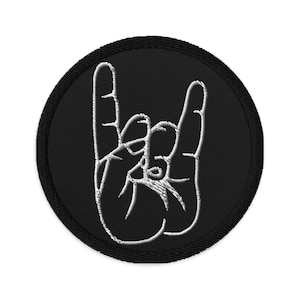 Może przedstawiać: Czarna naszywka haftowana z białym konturem dłoni wykonującej gest rock and roll.