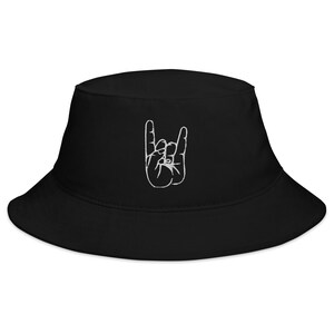 Puede incluir: Sombrero de cubo negro con un gesto de mano de rock and roll bordado en blanco.